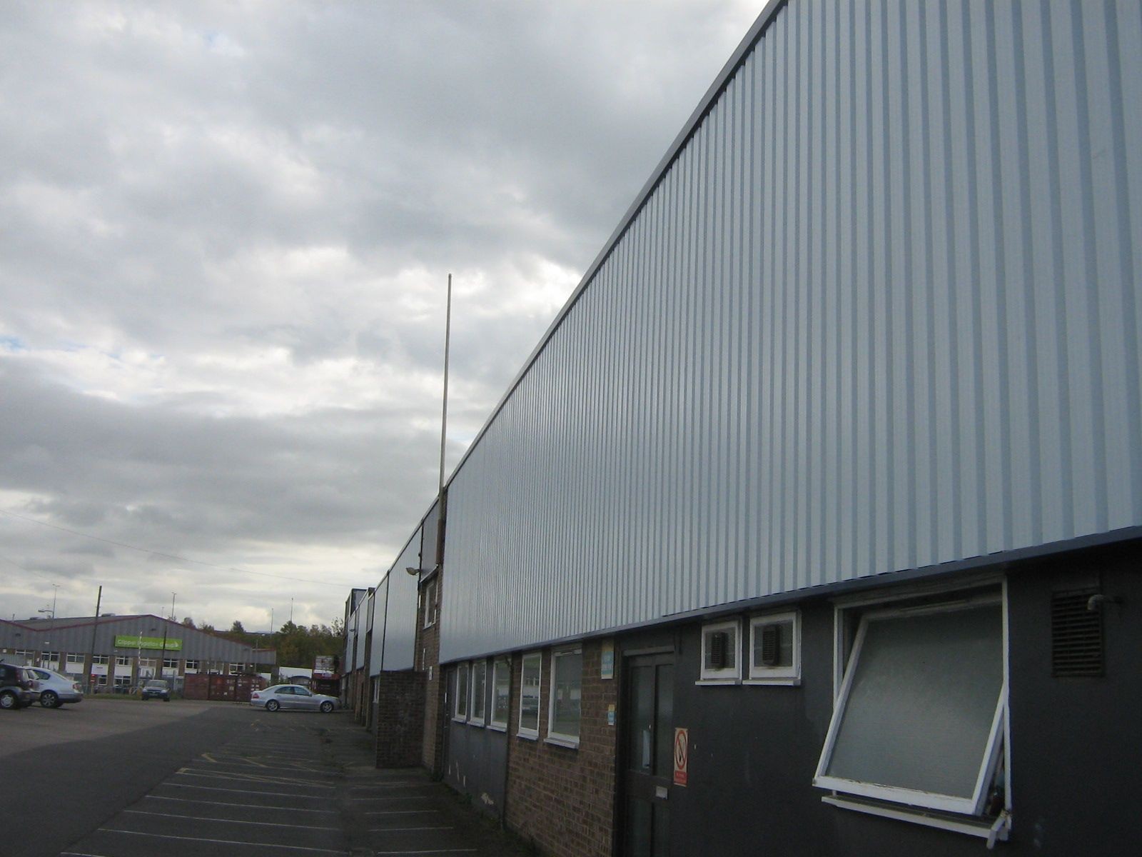 Exterior view of industrial buildings with corrugated metal siding and parking spaces under a cloudy sky.