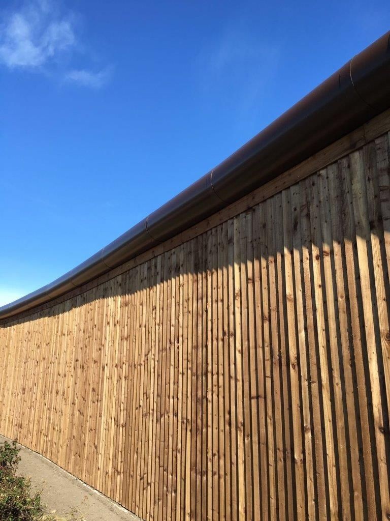 Long wooden fence with vertical slats under a clear blue sky.