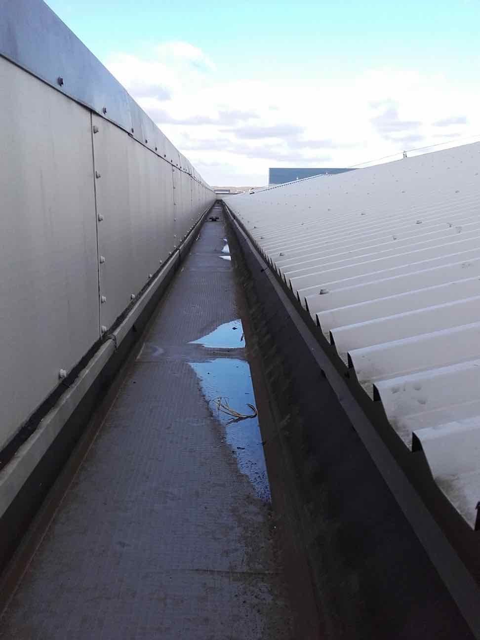 Narrow gap between two industrial building roofs, with puddles of water reflecting the sky.