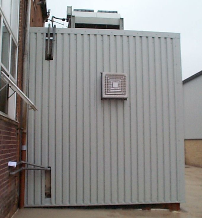 Metal-clad exterior of an industrial building with a vent and piping visible.